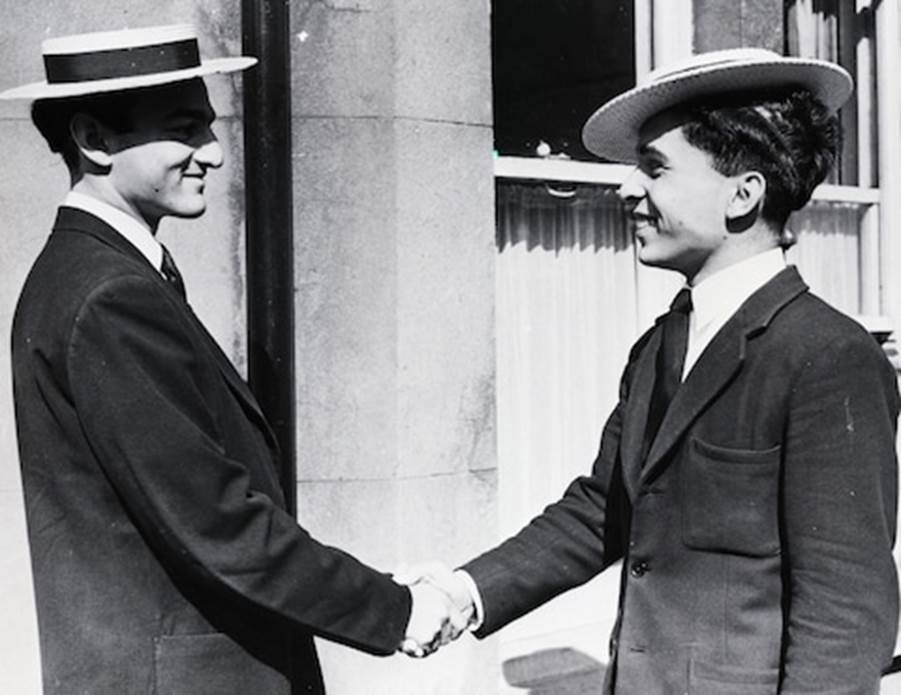 A person in a suit and hat shaking hands with another person in a suit  Description automatically generated with low confidence