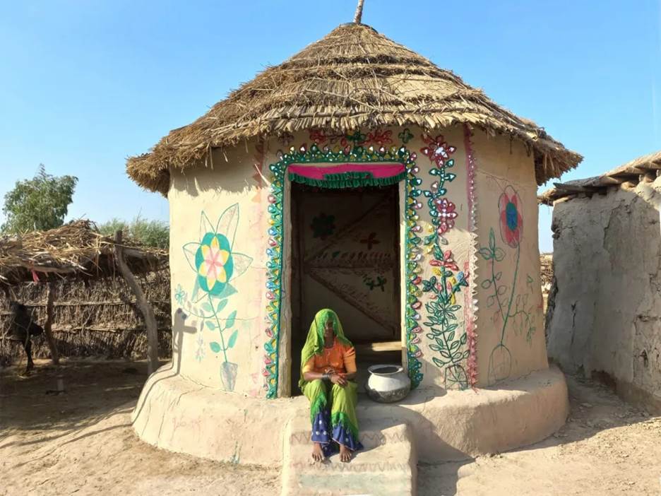 A woman sits on the front step of her home, built to Lari's bamboo, earth and lime designs.<span class=copyright>Heritage Foundation of Pakistan</span>