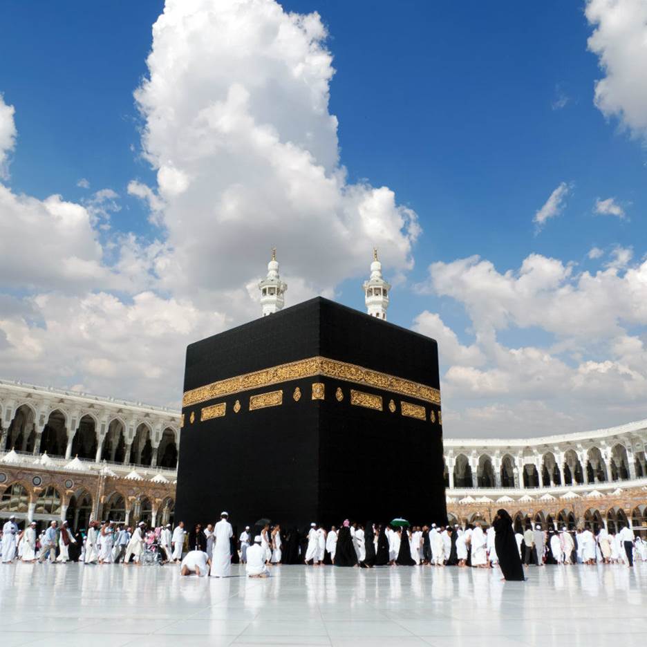 A group of people in white robes with Kaaba in the background  Description automatically generated with low confidence