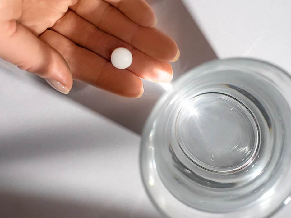 a pill in someone's hand, next to a glass of water