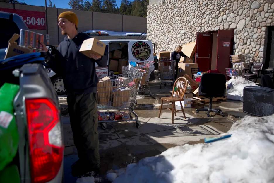 Jeremy Cote, an employee at Goodwin & Sons Market, and Bridgett Goodwin, one of the owners, carry out boxes after the roof caved in at the business, in Crestline, Calif., March 9, 2023. (Jenna Schoenefeld/The New York Times)