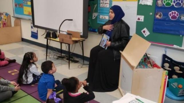 A person in a black dress sitting in a classroom Description automatically generated with low confidence