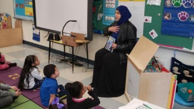 A person in a black dress sitting in a classroom  Description automatically generated with low confidence