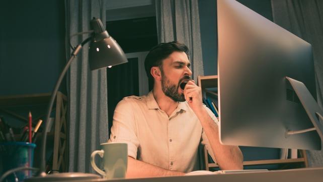 A person yawning in front of a computer Description automatically generated