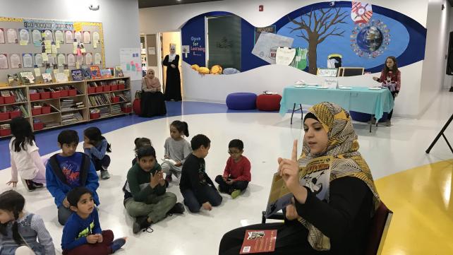 A person in a headscarf pointing at a group of children  Description automatically generated with low confidence