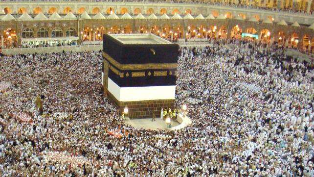 A large crowd of people around a black square structure with Kaaba in the background Description automatically generated with low confidence
