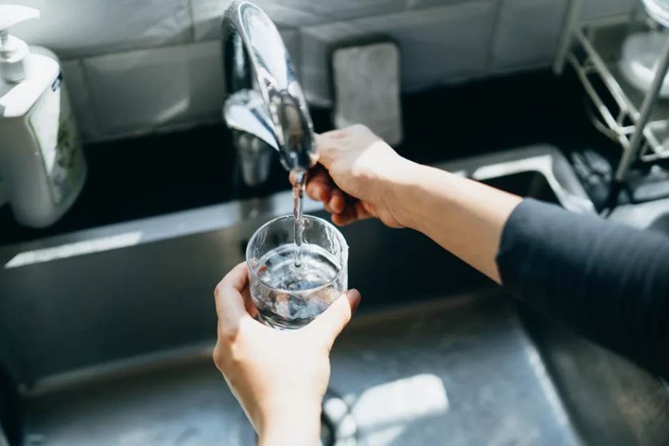 Someone using a faucet to pour water into a glass