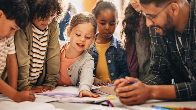 A group of children looking at a book  Description automatically generated