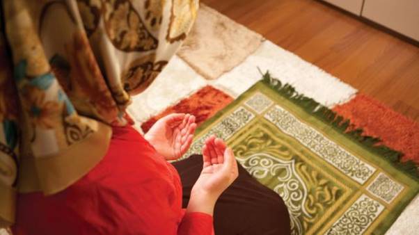 A person in a red shirt and a scarf praying Description automatically generated