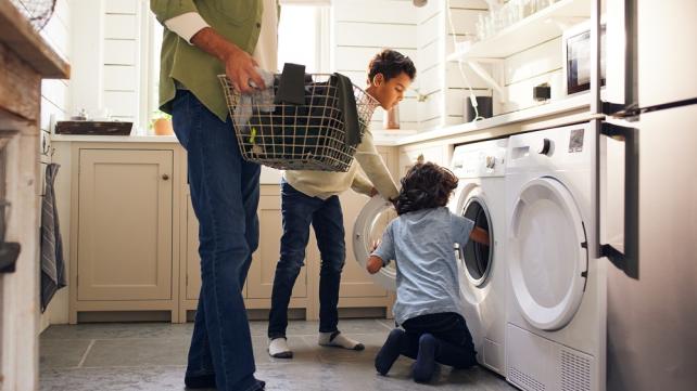 A person and two children looking at a washing machine Description automatically generated