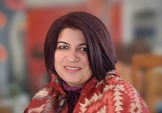 A person with dark hair wearing a red and white patterned jacket Description automatically generated