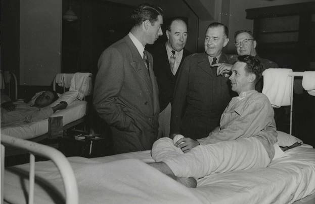 A person in a suit standing next to a person in a hospital bed AI-generated content may be incorrect.
