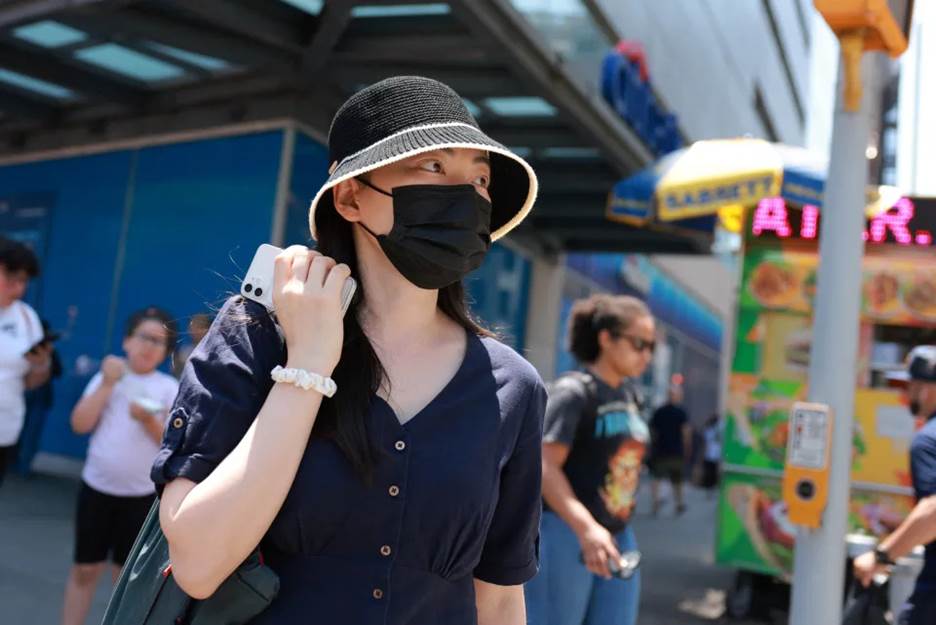 A woman in a hat and face mask on a sidewalk.