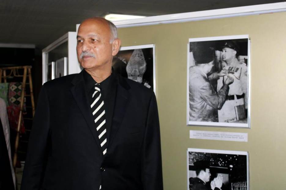 A person in a suit and tie standing in front of a wall with pictures Description automatically generated
