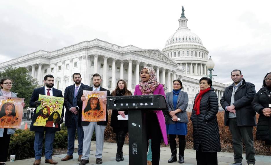 A group of people holding signs in front of a white building Description automatically generated with medium confidence
