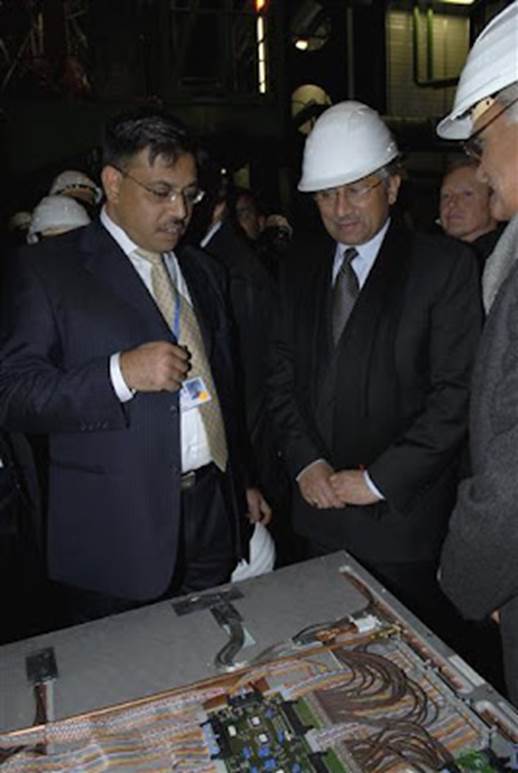 Men in a suit and white helmet looking at a table  Description automatically generated