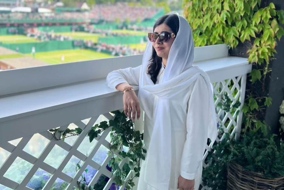 A person wearing a white dress and sunglasses leaning on a white railing Description automatically generated