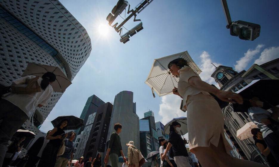 Pedestrians use umbrellas to shelter from the midday sun as they cross a street during heatwave conditions in Tokyo on July 18, 2023. — AFP