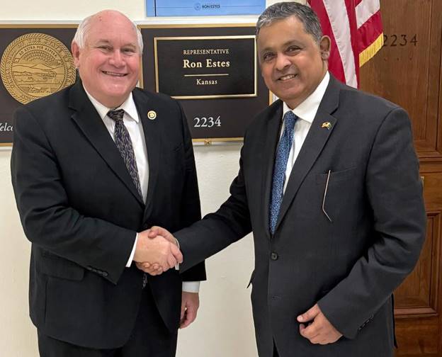 Two men shaking hands in front of a flag Description automatically generated