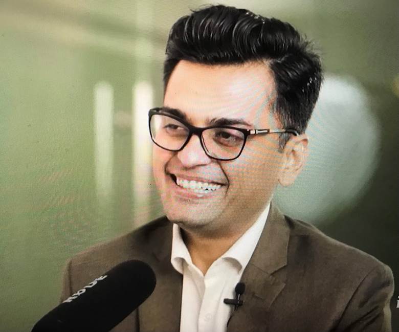 A person wearing glasses and a suit Description automatically generated