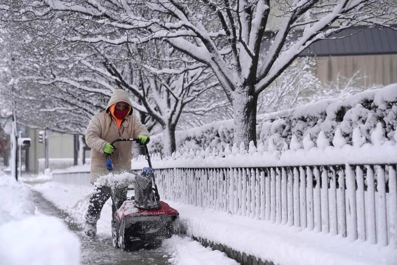 A person clears snow off a sidewalk with a snow blower.