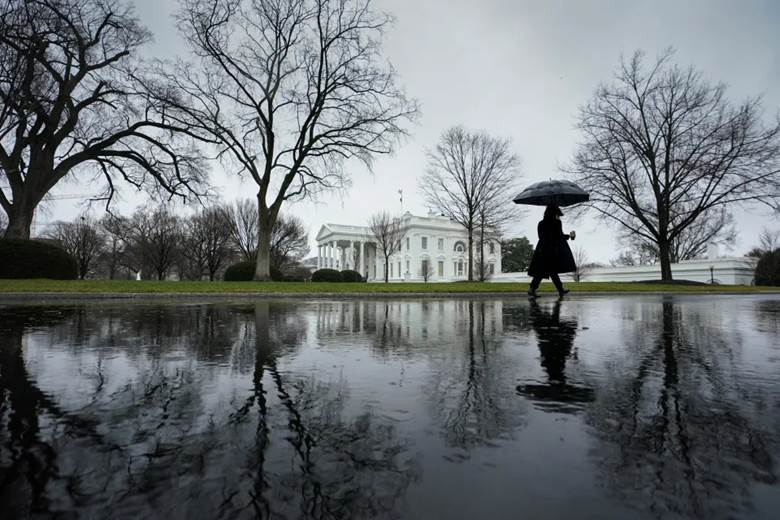 Someone holding an umbrella walks up the driveway toward the White House.
