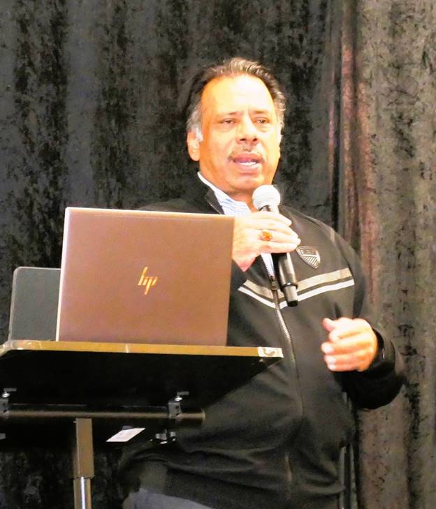 A person standing at a podium with a microphone and a computer  Description automatically generated