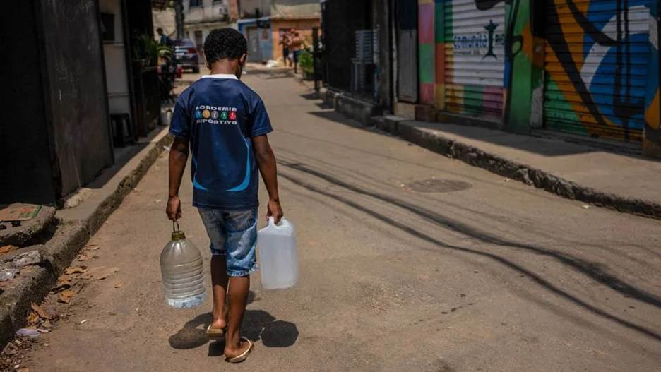 A person carrying two plastic jugs on a street  Description automatically generated