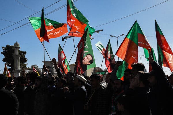 Protesters in shadow holding flags with images of Imran Khan and variations of the Pakistani flag.