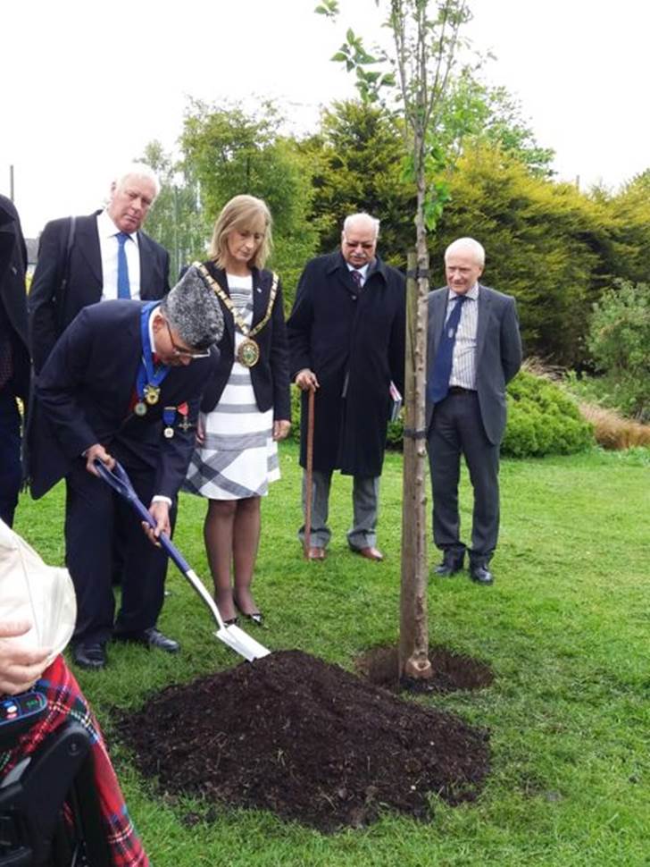 Shera, while wearing a Pakistani Jinnah cap, plants a friendship tree in the borough of Rugby at a 2017 ceremony conferring him with the honor Freedom of the Borough of Rugby for his dedication to the borough and to building bridges. A delegation, including former Pakistani High Commissioner Wajid Shamsul Hasan, looks on.