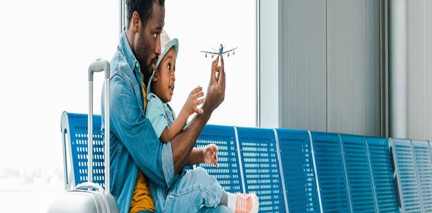 Parent holding their toddler and a toy airplane at the airport 