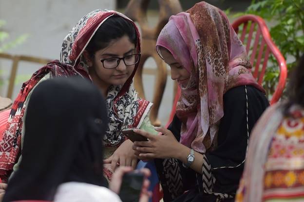 A group of women wearing headscarves looking at a book  Description automatically generated