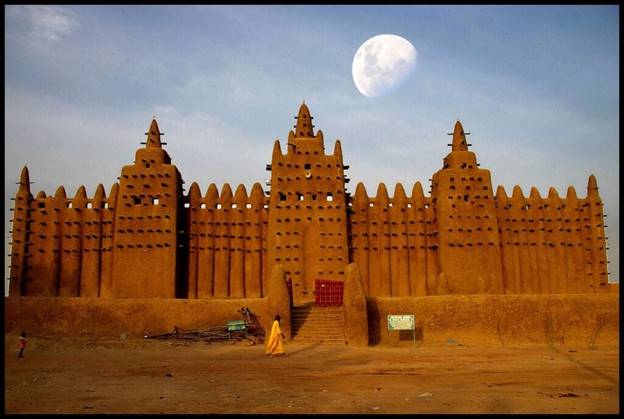 A large building with a moon in the background with Great Mosque of Djenné in the background Description automatically generated