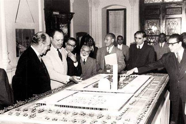 A group of men looking at a model of a building Description automatically generated